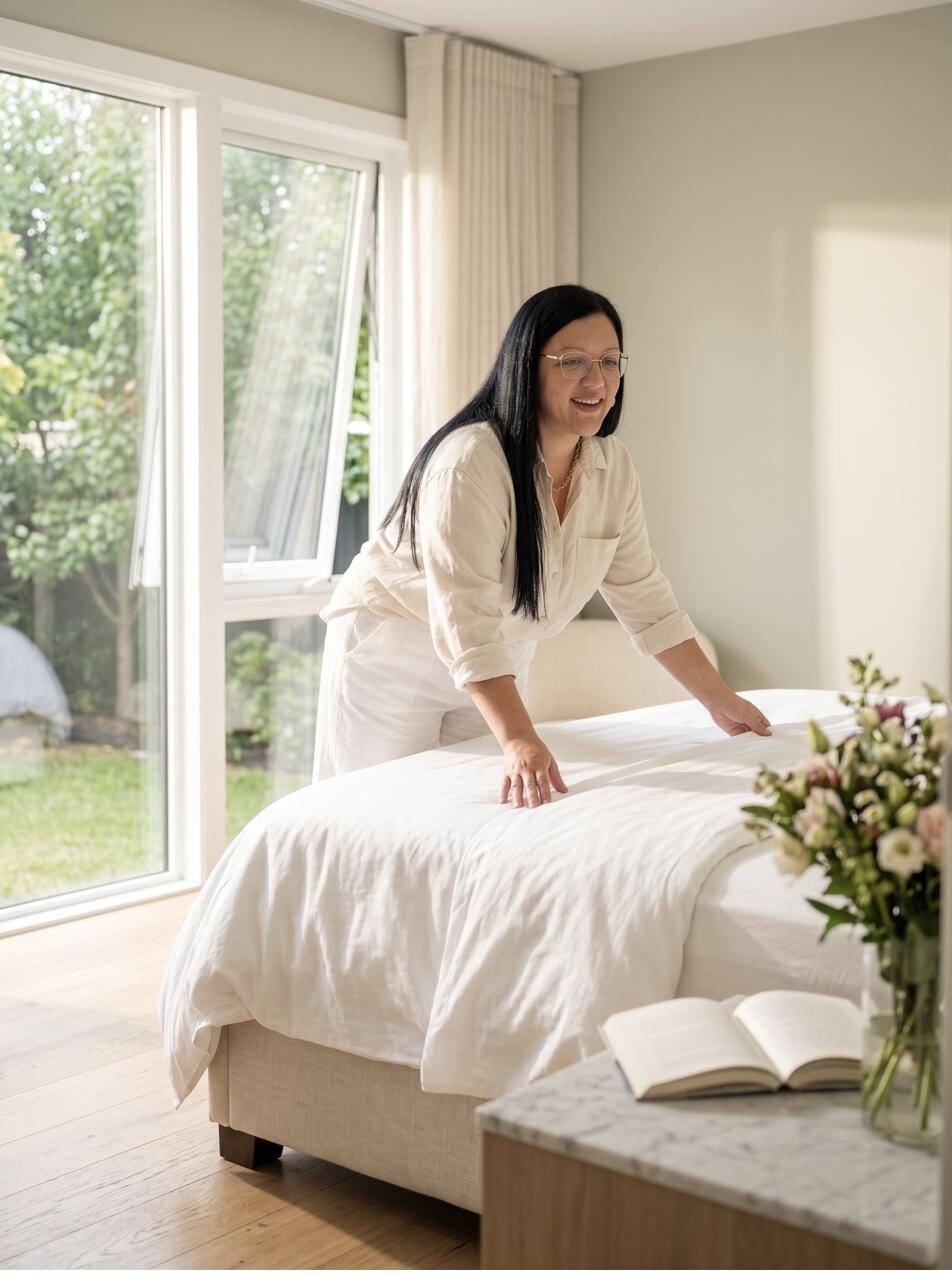 Bed dressed with crisp white linen beside a vase of flowers
